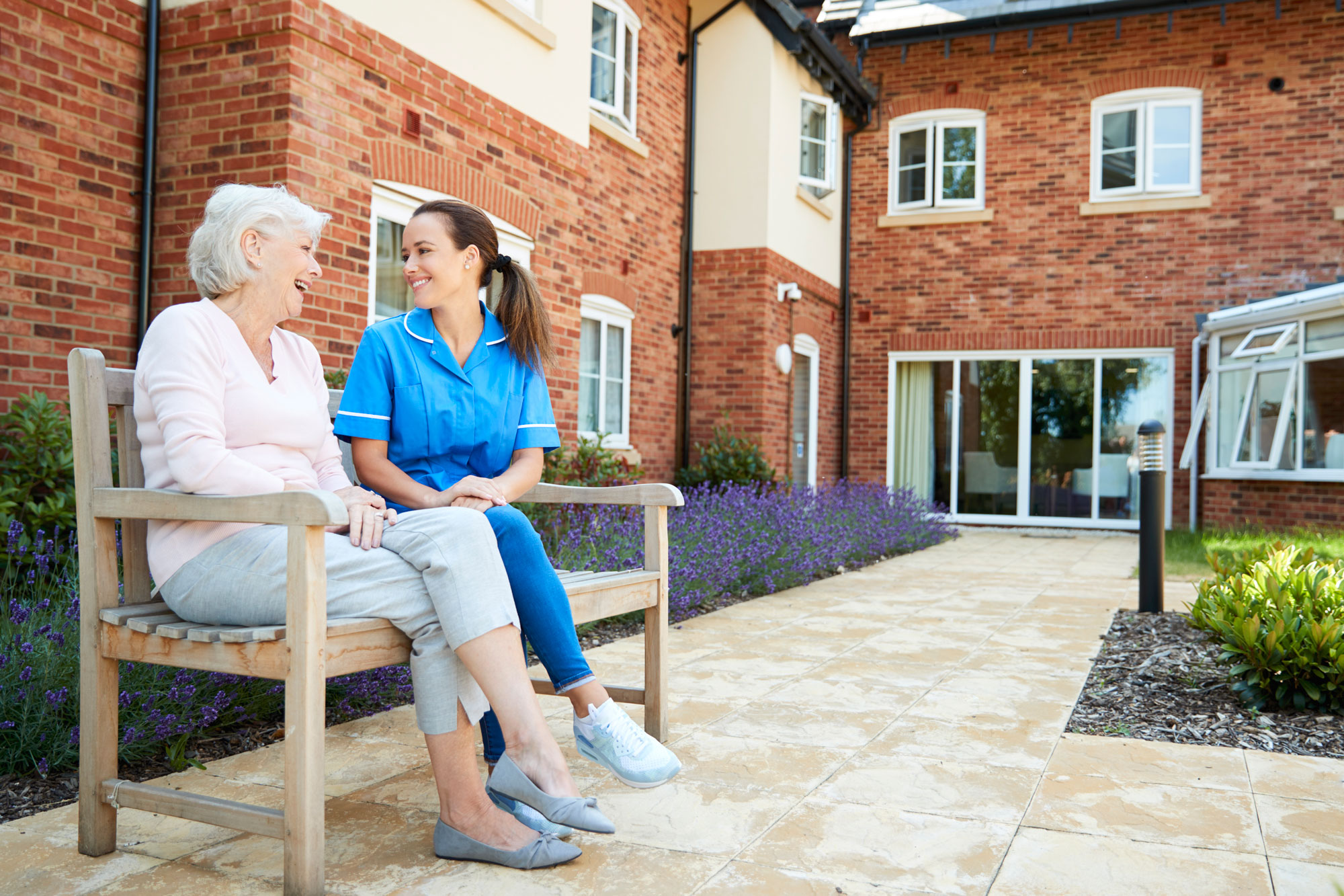 senior-woman-sitting-bench-talking-with-nurse-retirement-home-edited